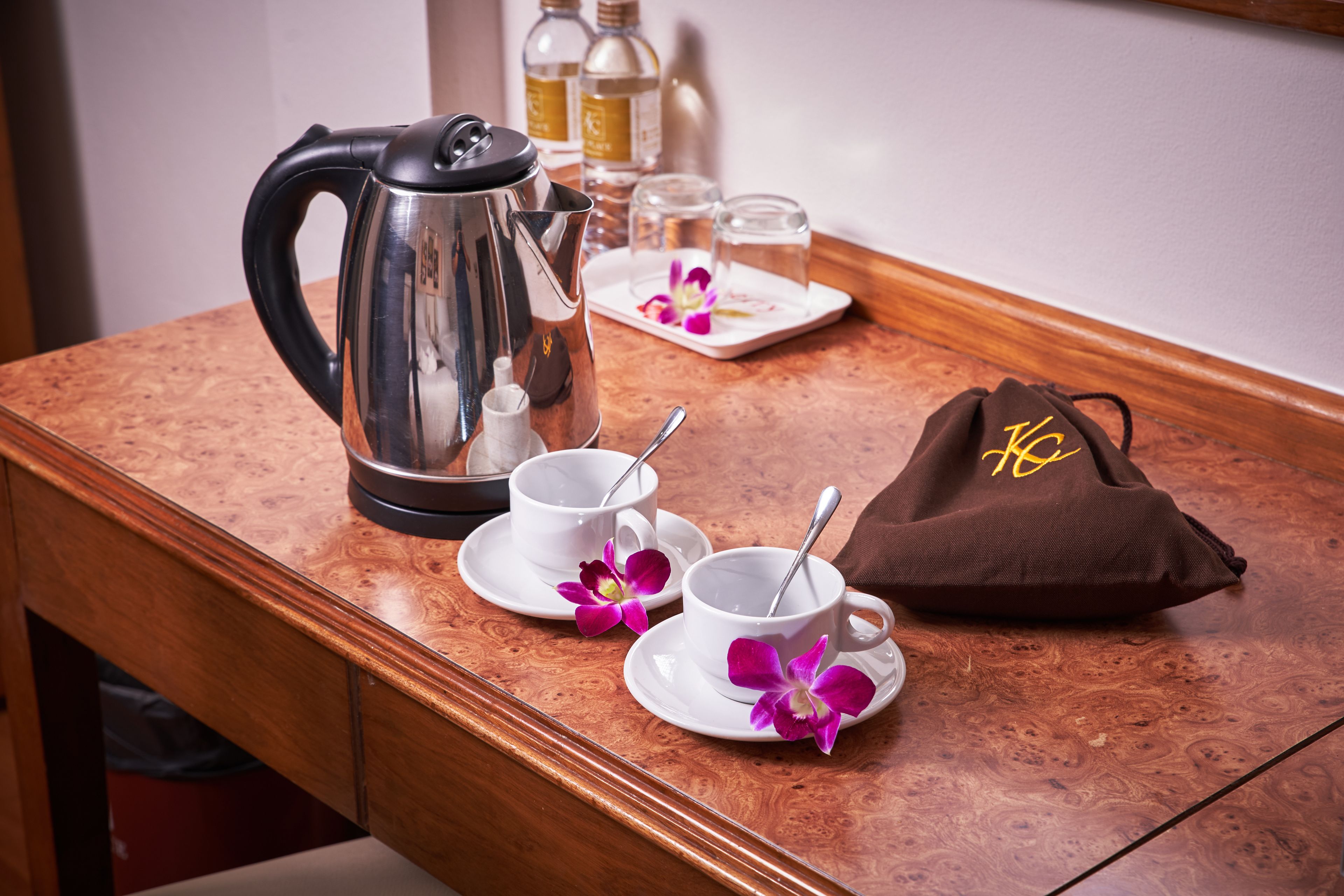 A wooden table with a coffee pot, two white cups with saucers, a brown bag, and a small plate with a flower and a spoon.