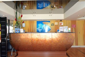 A hotel reception desk with a large 'City Park Hotel' sign, a plant on the left, and a 'Fire Door Do Not Obstruct' sign on the right. - City Park Hotel (South Melbourne)