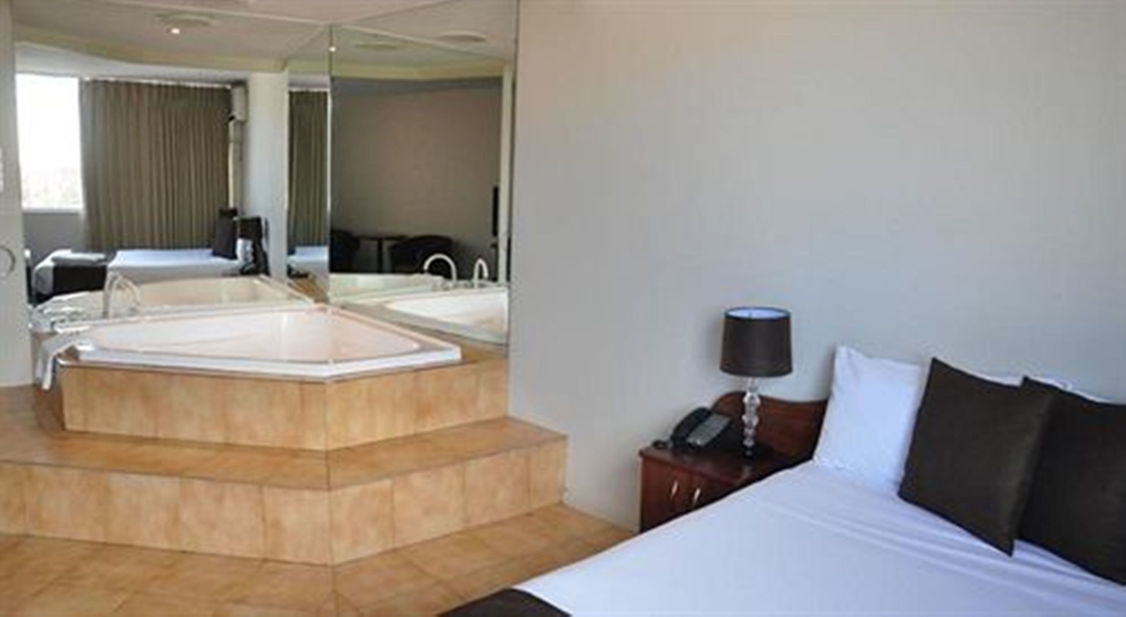 Une chambre d’hôtel avec une grande baignoire, un lit, une table de chevet avec une lampe et un miroir.