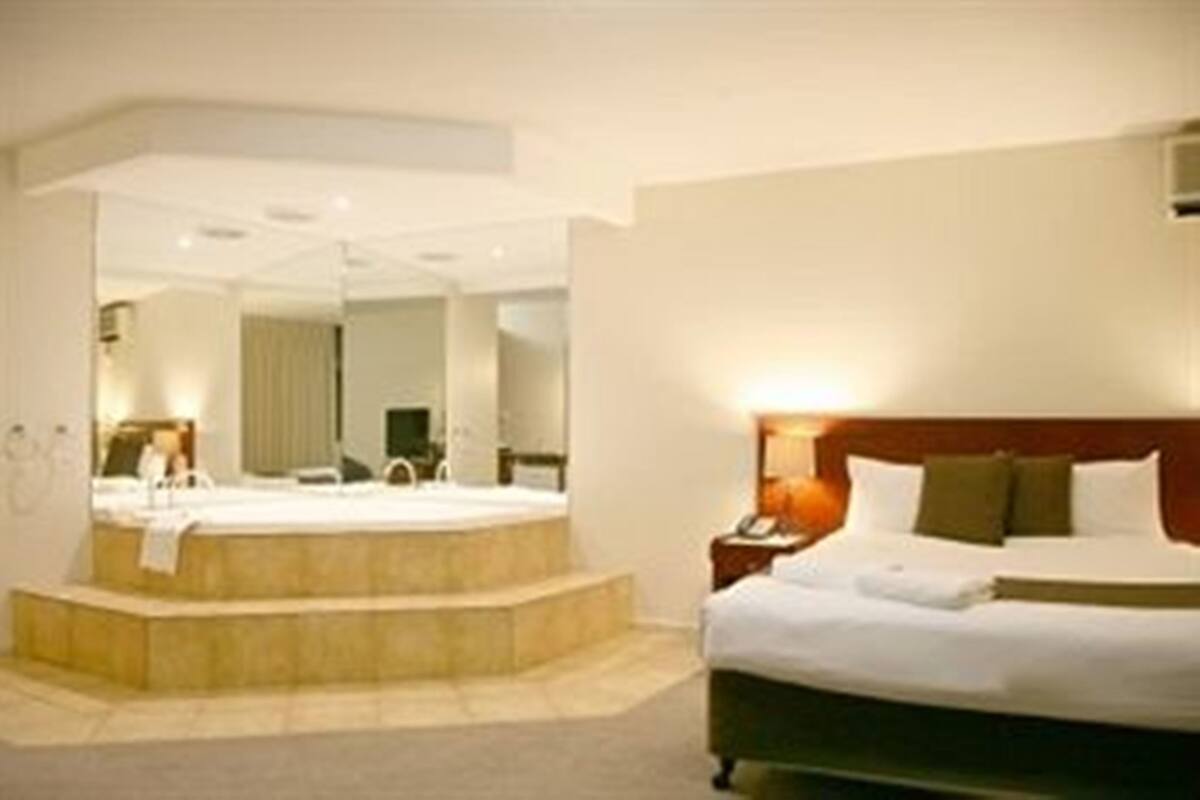 A hotel room with a bed, a nightstand, a mirror, and a bathroom with a bathtub.