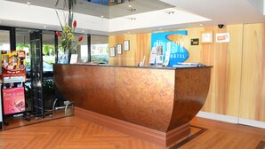 Una recepción de hotel con detalles de madera, un jarrón grande con flores y un cartel del Hotel CityPark.