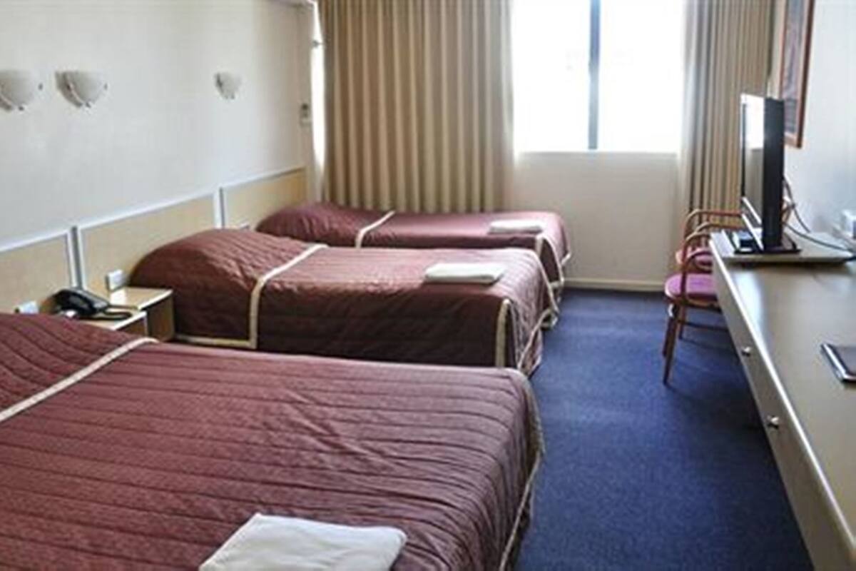 A hotel room with three beds, a desk with a computer, and a window with curtains.