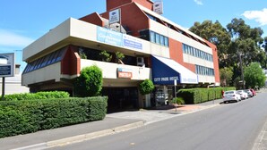Un edificio de varios pisos con restaurante y salón de conferencias en la planta baja, un cartel de hotel en la parte superior, y un estacionamiento con coches.