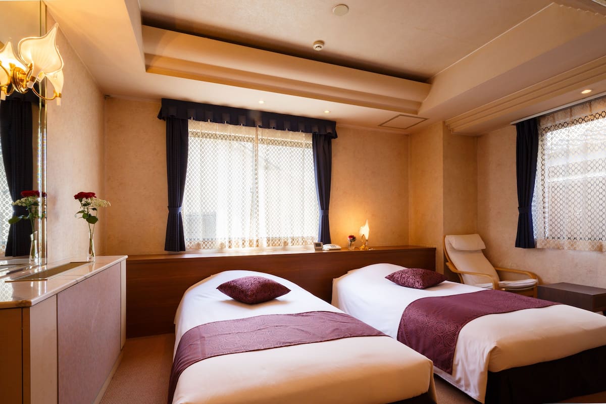 A hotel room with two beds, a desk, a chair, and a window with curtains.