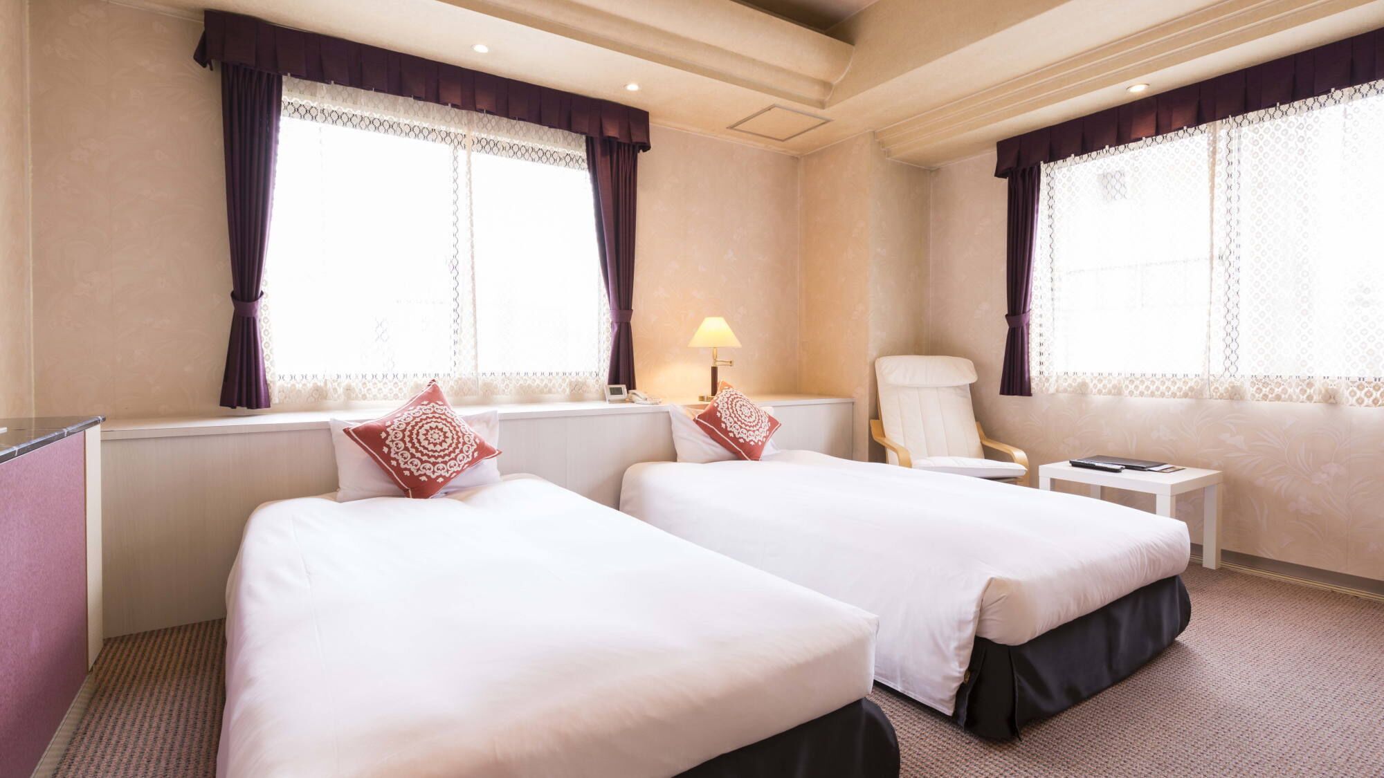 A hotel room with two beds, a chair, a nightstand, and a lamp.