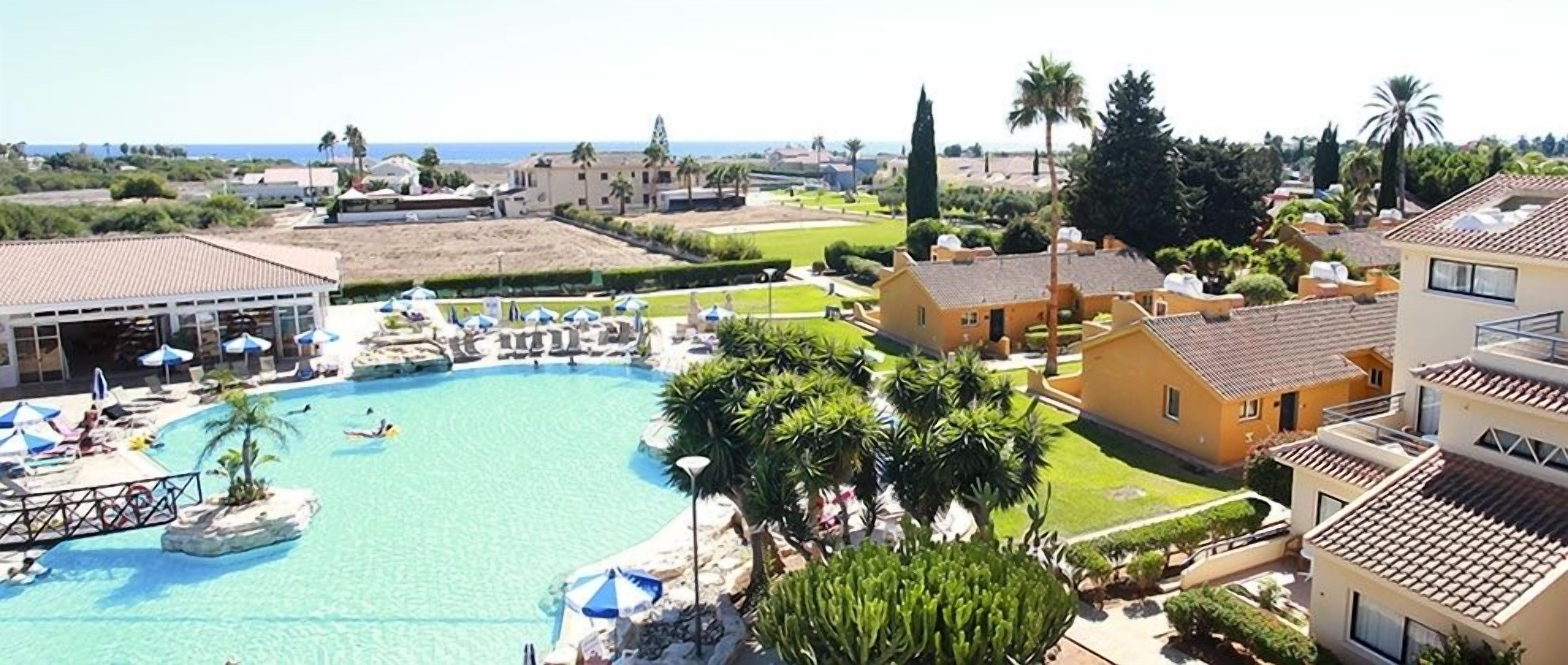 Een resort met een groot zwembad, ligbedden en uitzicht op zee.
