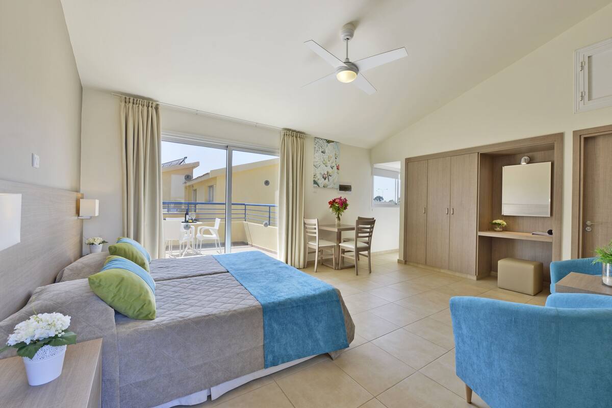 Une chambre d’hôtel équipée d’un lit, d’un bureau, d’une chaise, d’un balcon et d’un ventilateur de plafond.