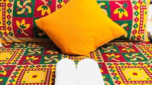 A bed with a colorful patterned bedspread, a rolled white towel, and a potted plant with red flowers. - Delta Lounge (Kowloon)