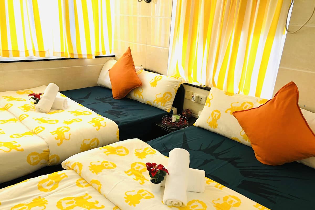 Quarto de hotel com duas camas, cada uma com roupa de cama estampada em amarelo e branco, almofadas laranja e uma pequena mesa com um vaso de flores.