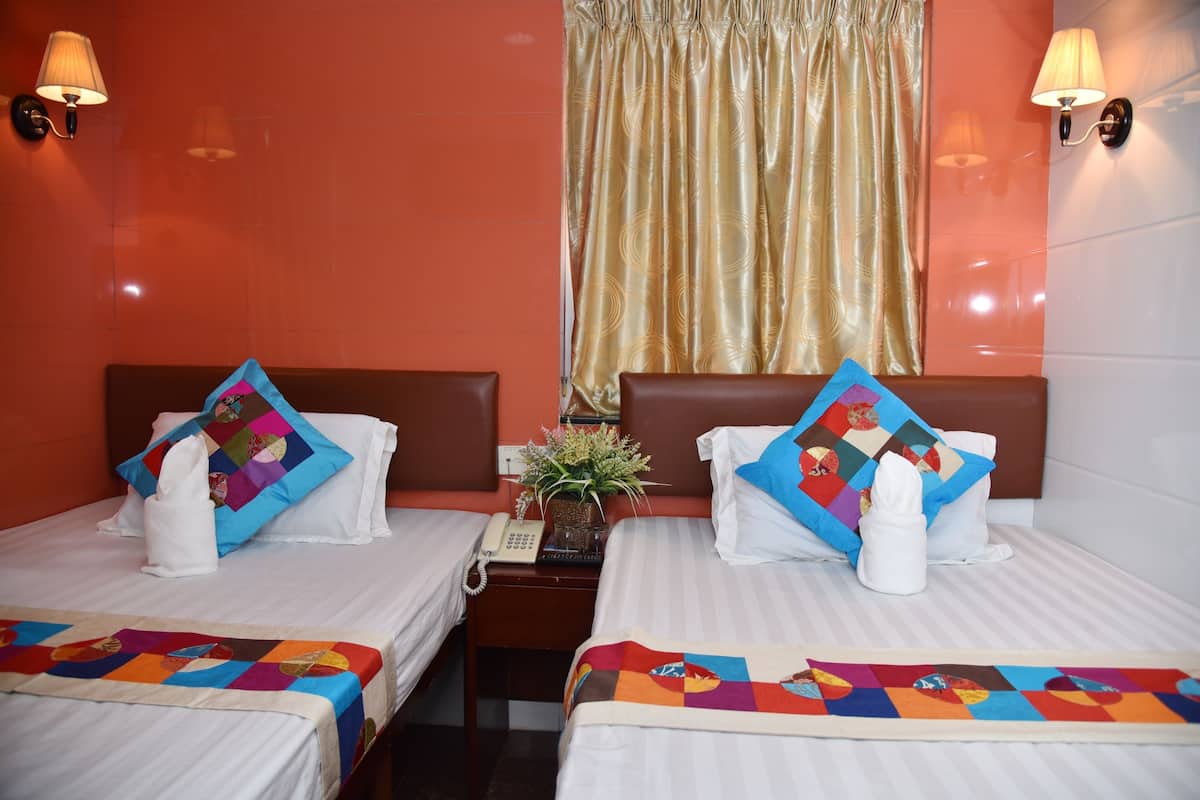 Quarto de hotel com duas camas, cada uma com um edredom colorido, uma mesinha com telefone e uma planta.