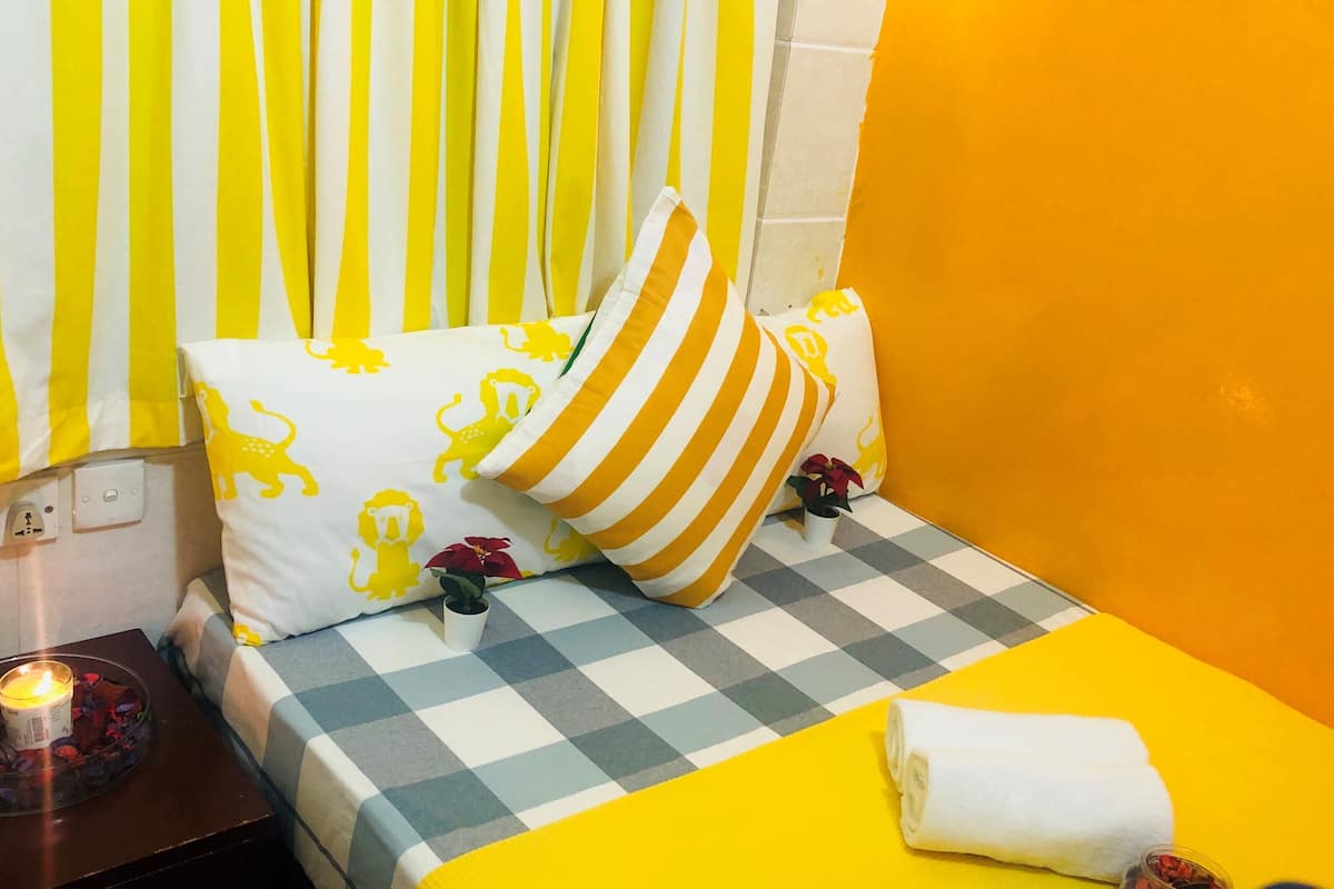 Uma cama com colcha xadrez, almofadas listradas e parede amarela.