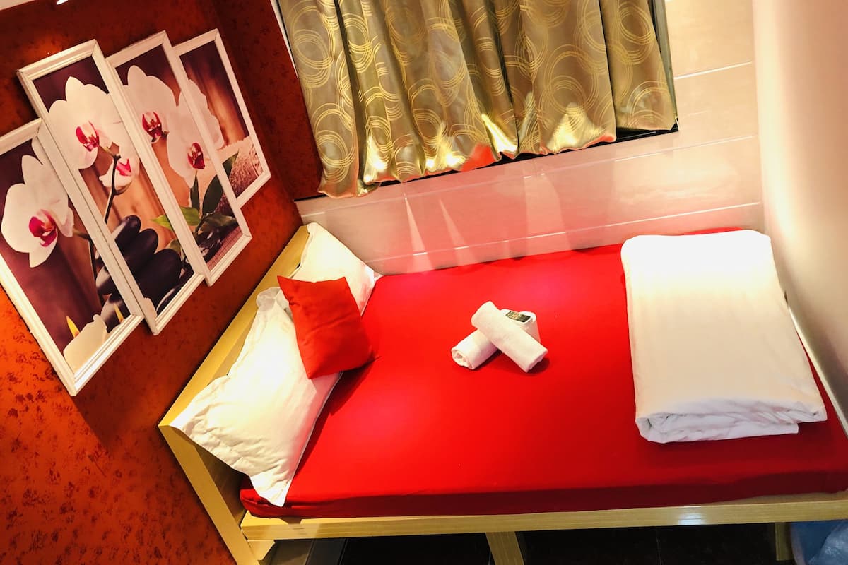 Quarto de hotel com colcha vermelha, almofadas brancas e vermelhas, uma toalha enrolada e um quadro com flores na parede.