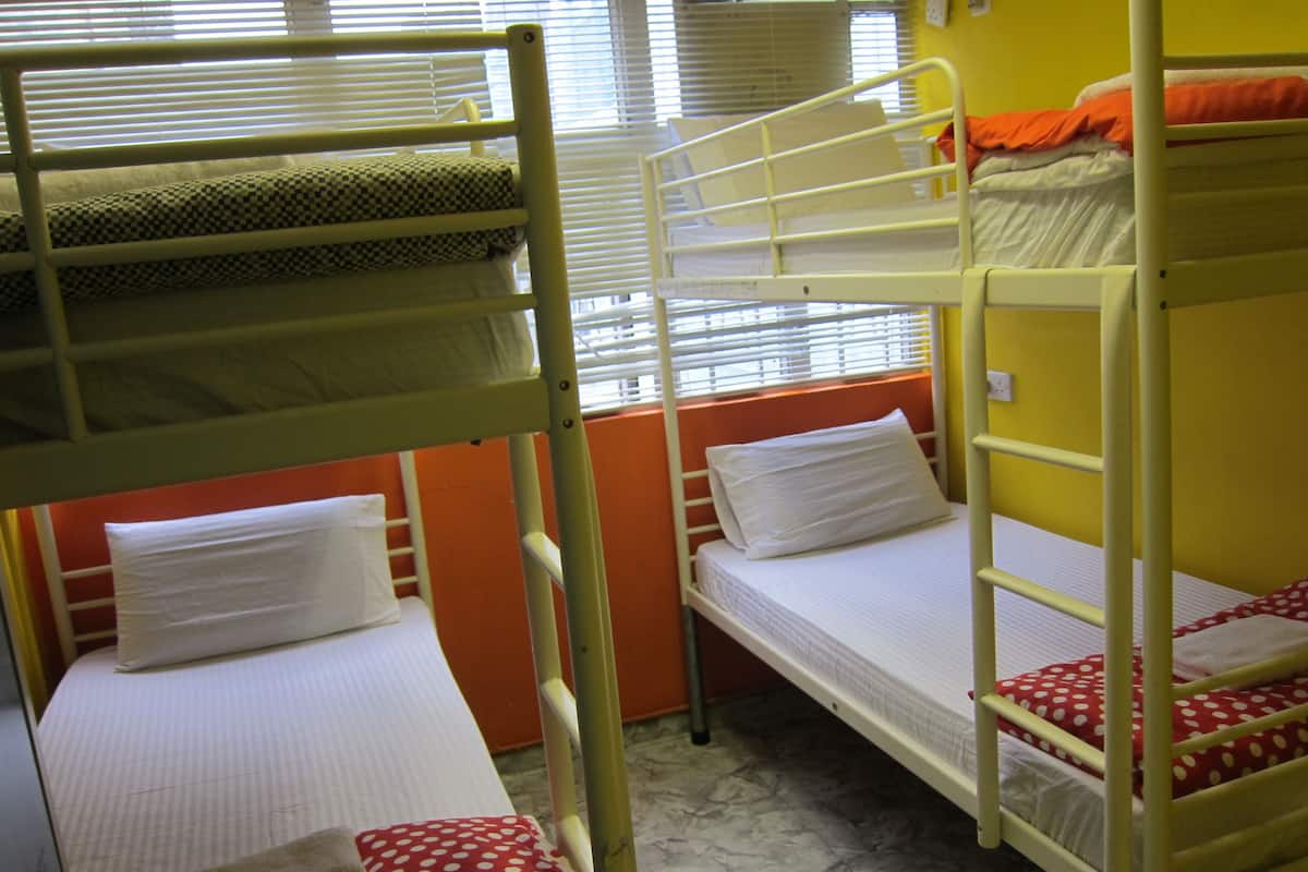 Um dormitório com beliches, uma janela com cortinas e uma parede amarela.