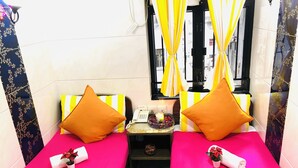 A small hotel room with two beds, each with a pink and yellow striped bedspread, and matching pillows. There is a small table with a phone and a bowl of fruit between the beds. - Delta Lounge (Kowloon)