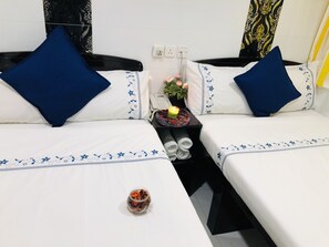 A double bed with blue pillows and a bedside table with a phone, a candle, and a glass jar of dried flowers. - Ashoka Hostel (Kowloon)