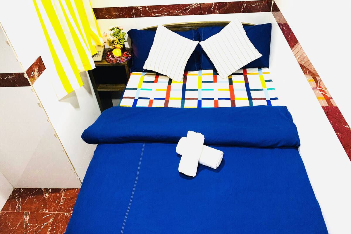 Een hotelkamer met een bed, nachtkastje, lamp en een potplant.