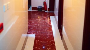 A hotel corridor with a marble floor, wall sconces, a fire extinguisher, and a trash bin. - Ashoka Hostel (Kowloon)