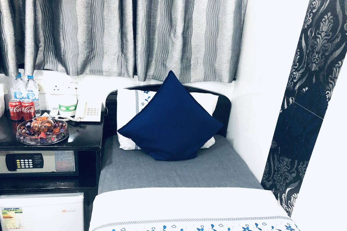Een hotelkamer met een bed, een bureau met telefoon, een koelkast en een raam met gordijnen.