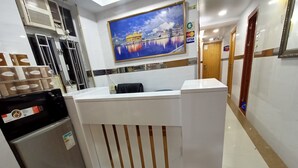 A reception desk with a refrigerator, a painting of a building, and a corridor with doors. - Ashoka Hostel (Kowloon)