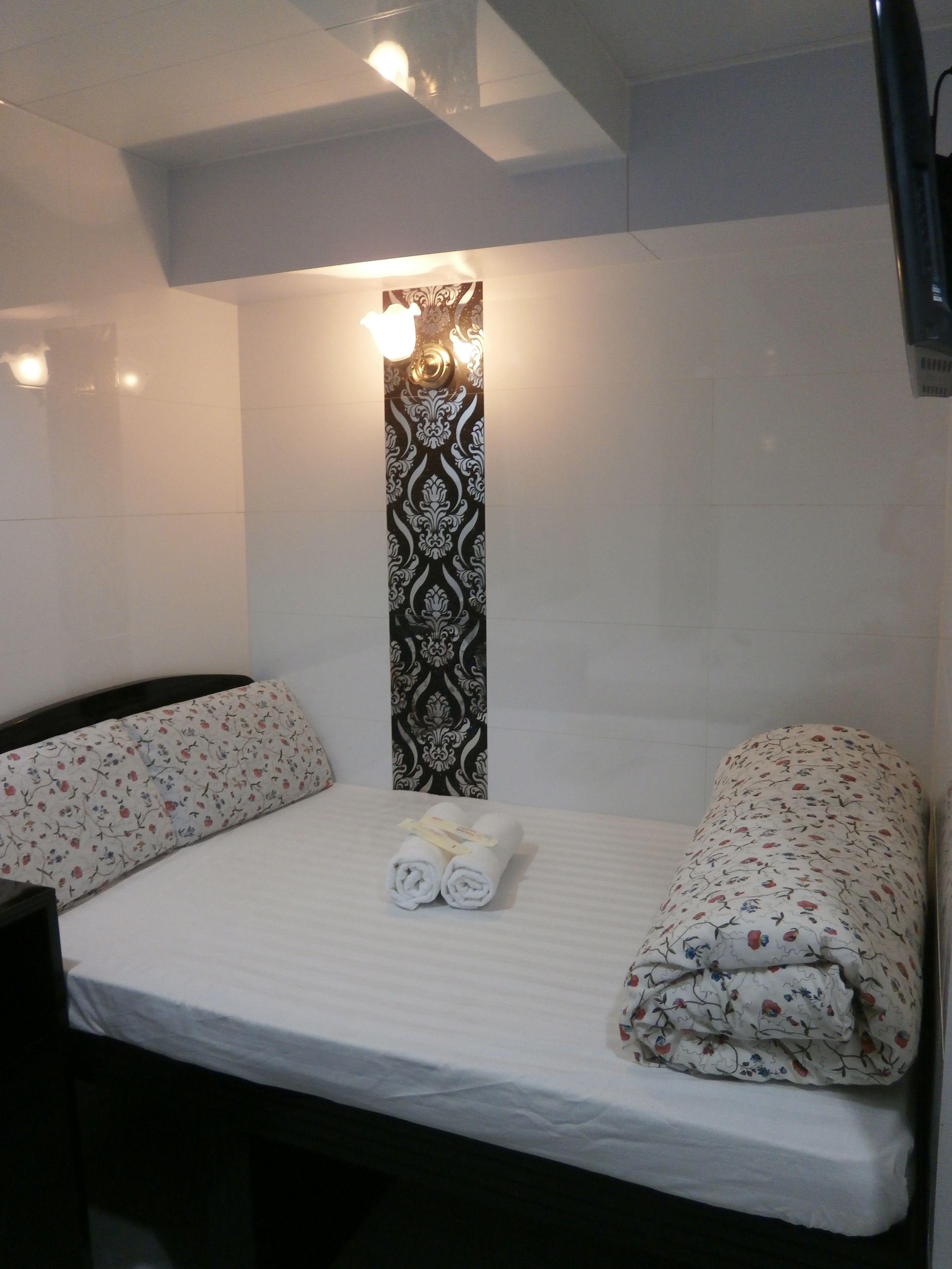 A small, single-bed room with a patterned wall, a bedside table, and a nightstand.