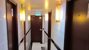 A hotel corridor with doors, a tiled floor, and wall-mounted lights. - Ashoka Hostel (Kowloon)