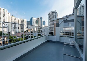 A balcony with a metal chair and a table, overlooking a cityscape with tall buildings. - Boxpackers Pratunam Hotel (Bangkok)
