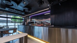 Zona de bar moderna con mostrador de acero inoxidable, asientos y vistas al exterior.