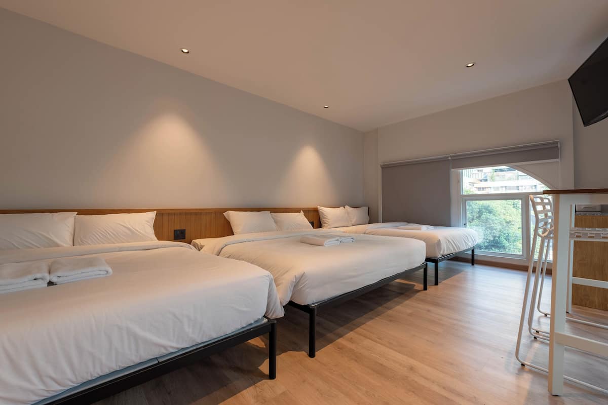 A hotel room with three beds, a TV, and a window with a view of buildings.