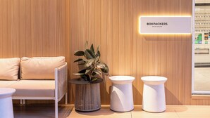Un interior moderno con una pared de madera, un sofá, una planta en maceta y dos mesitas blancas.