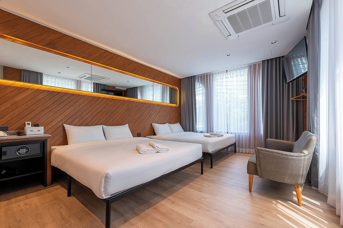 A hotel room with two beds, a chair, a desk, and a TV.