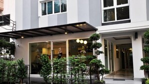 A modern building with a covered entrance, potted plants, and a visible interior with a dining area. - Delight Residence (Bangkok)