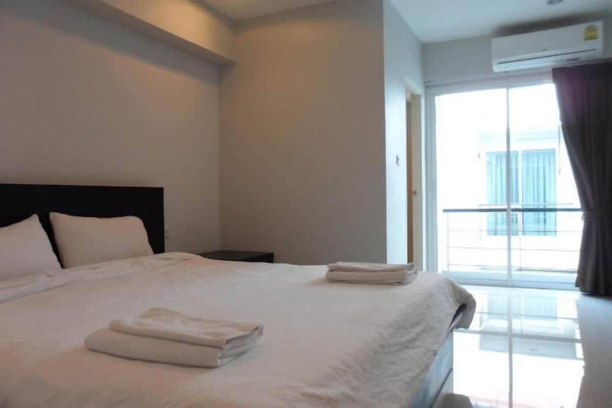 A hotel room with a large bed, a nightstand, a window with curtains, and an air conditioning unit.