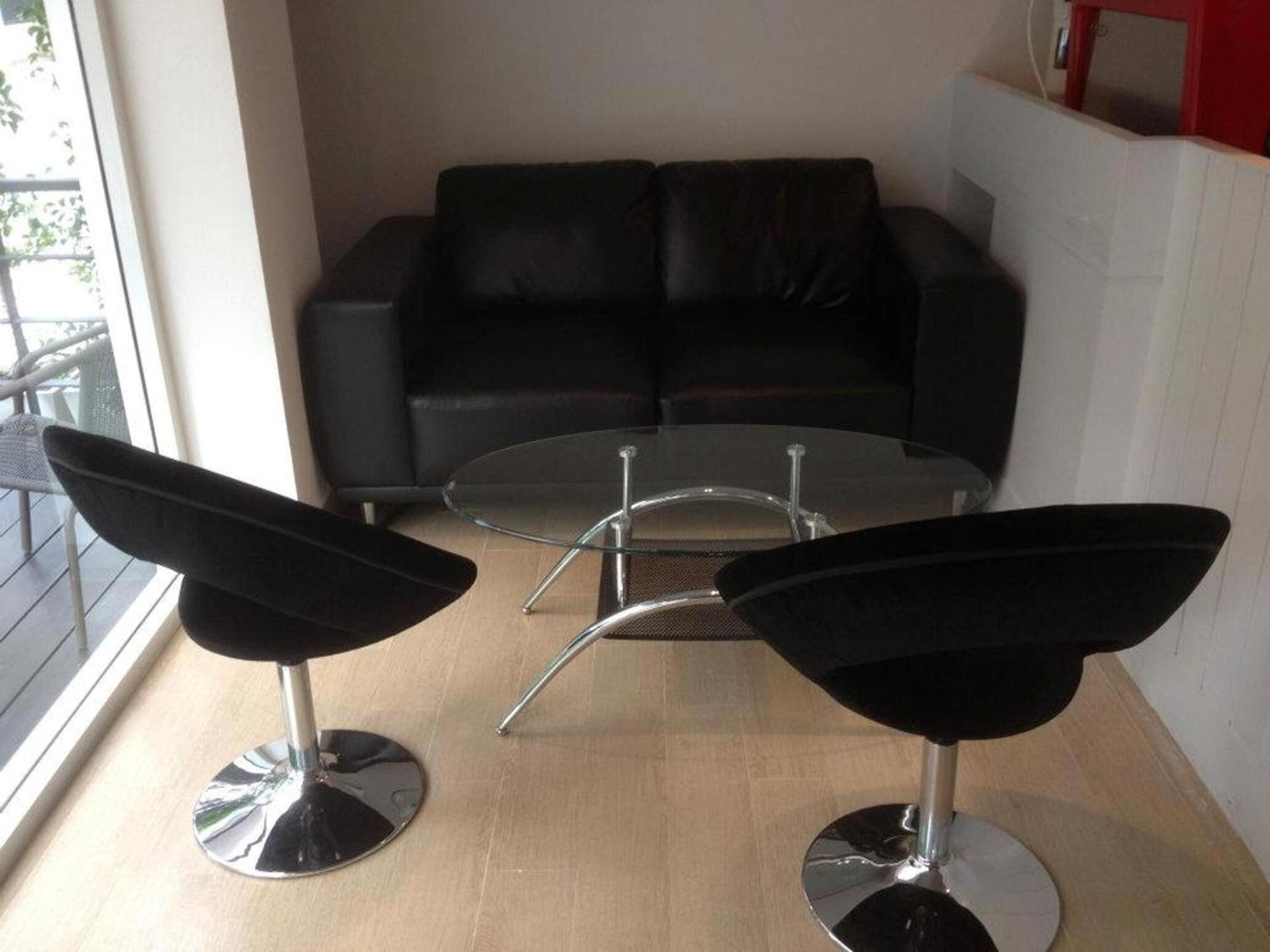 A modern living room with a black leather sofa, two black bar stools, and a glass coffee table.