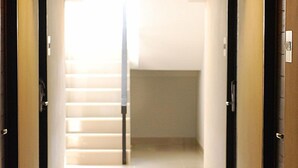 A hallway with a light-colored floor, a central staircase, and doors on either side. - Delight Residence (Bangkok)