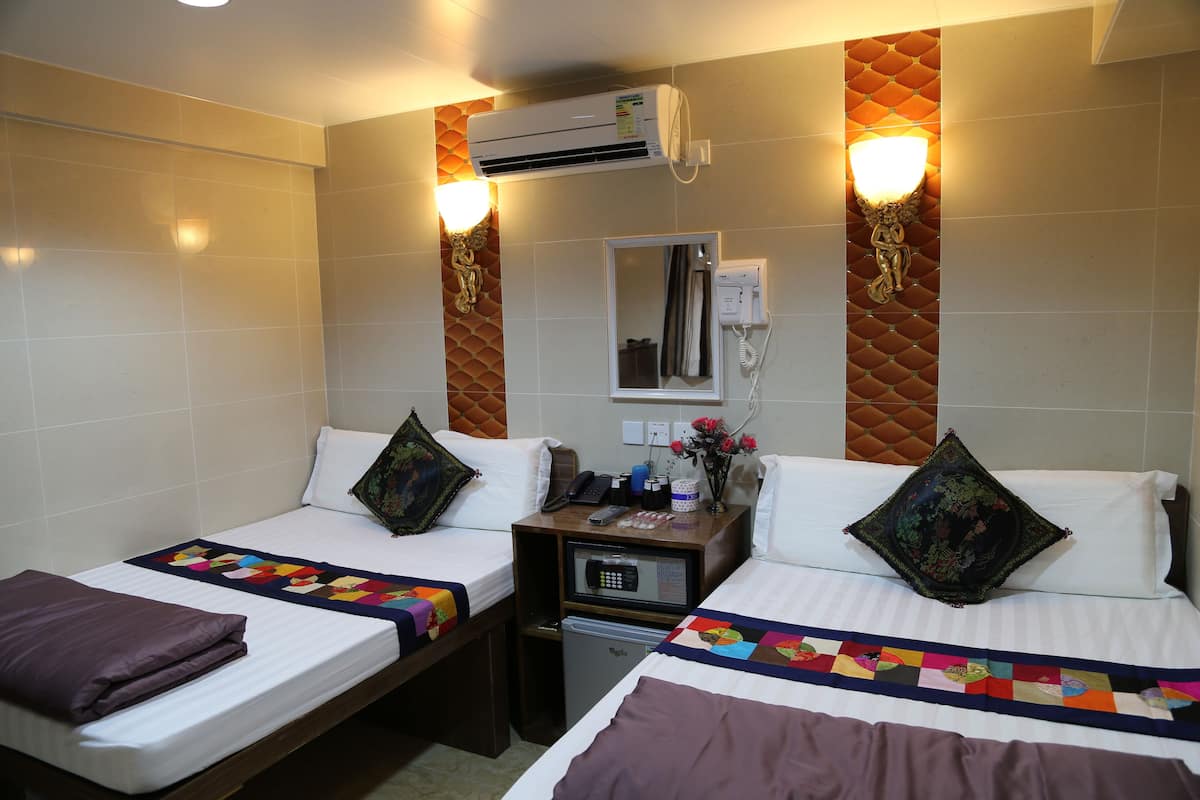 A hotel room with two beds, a small desk with a phone, a mirror, and an air conditioning unit.