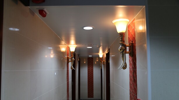 A hallway with tiled walls, recessed lighting, and wall-mounted sconces. - Australian Guest House (Kowloon)