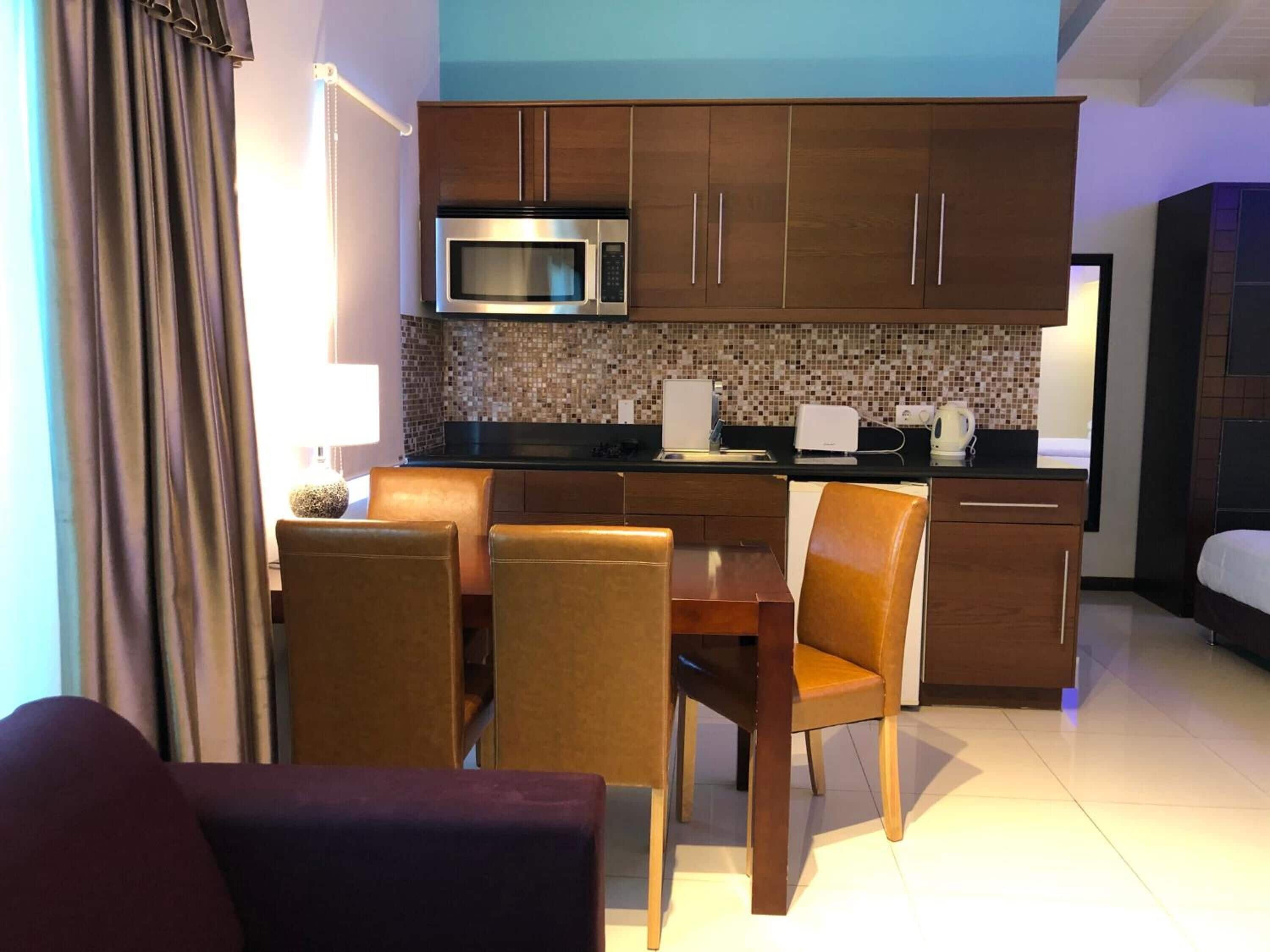A compact hotel room with a kitchenette, a dining area with a table and chairs, and a bed.