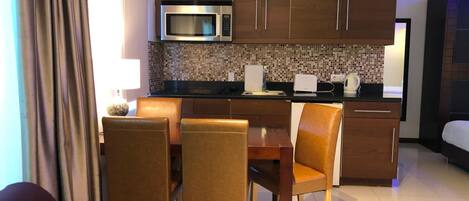 A compact hotel room with a kitchenette, a dining area with a table and chairs, and a bed.