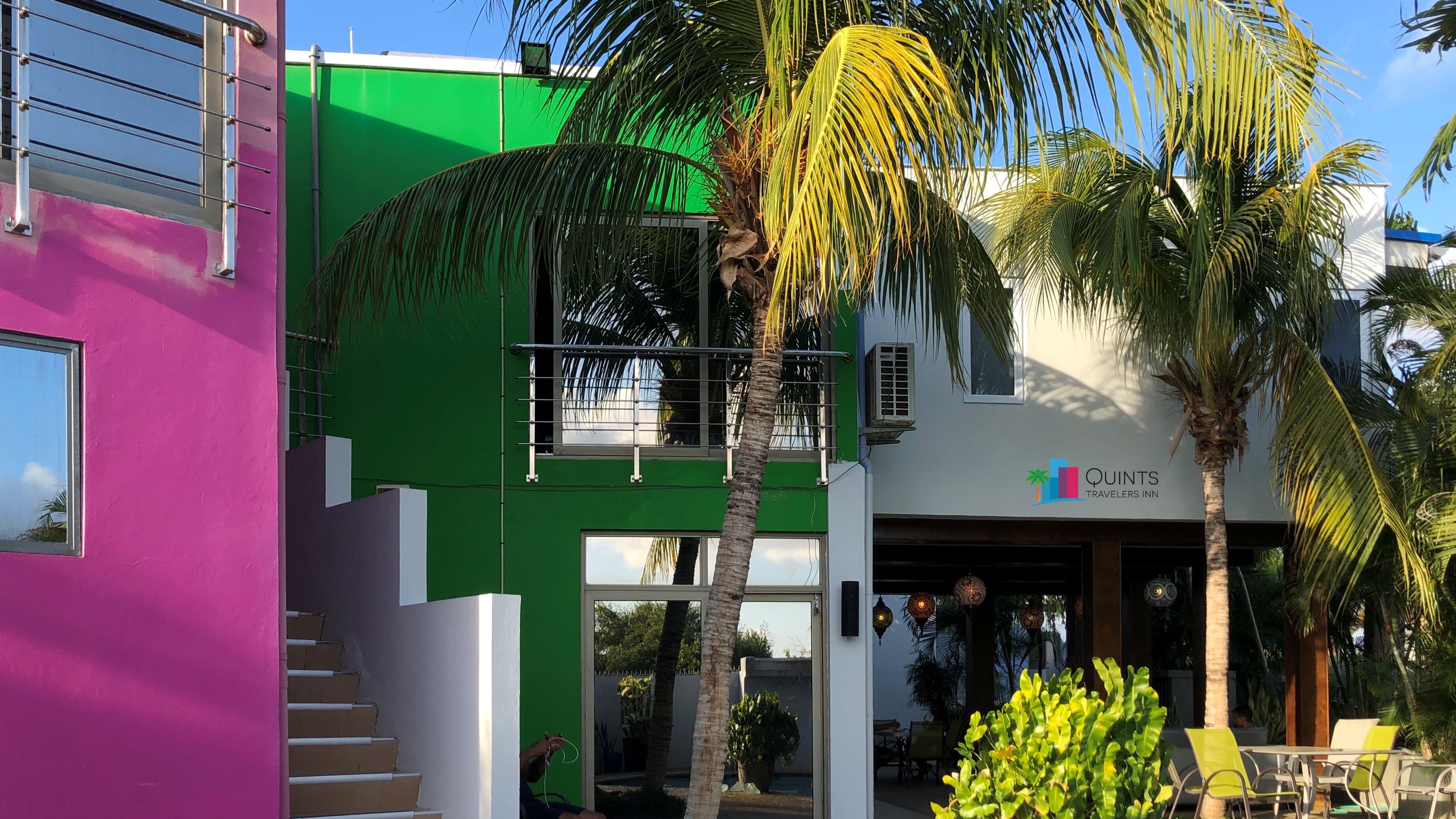 A modern building with a green and white facade, a visible balcony, and a sign for Quints Travelers Inn.