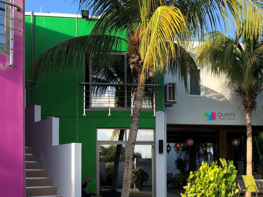 A modern building with a green and white facade, a visible balcony, and a sign for Quints Travelers Inn.