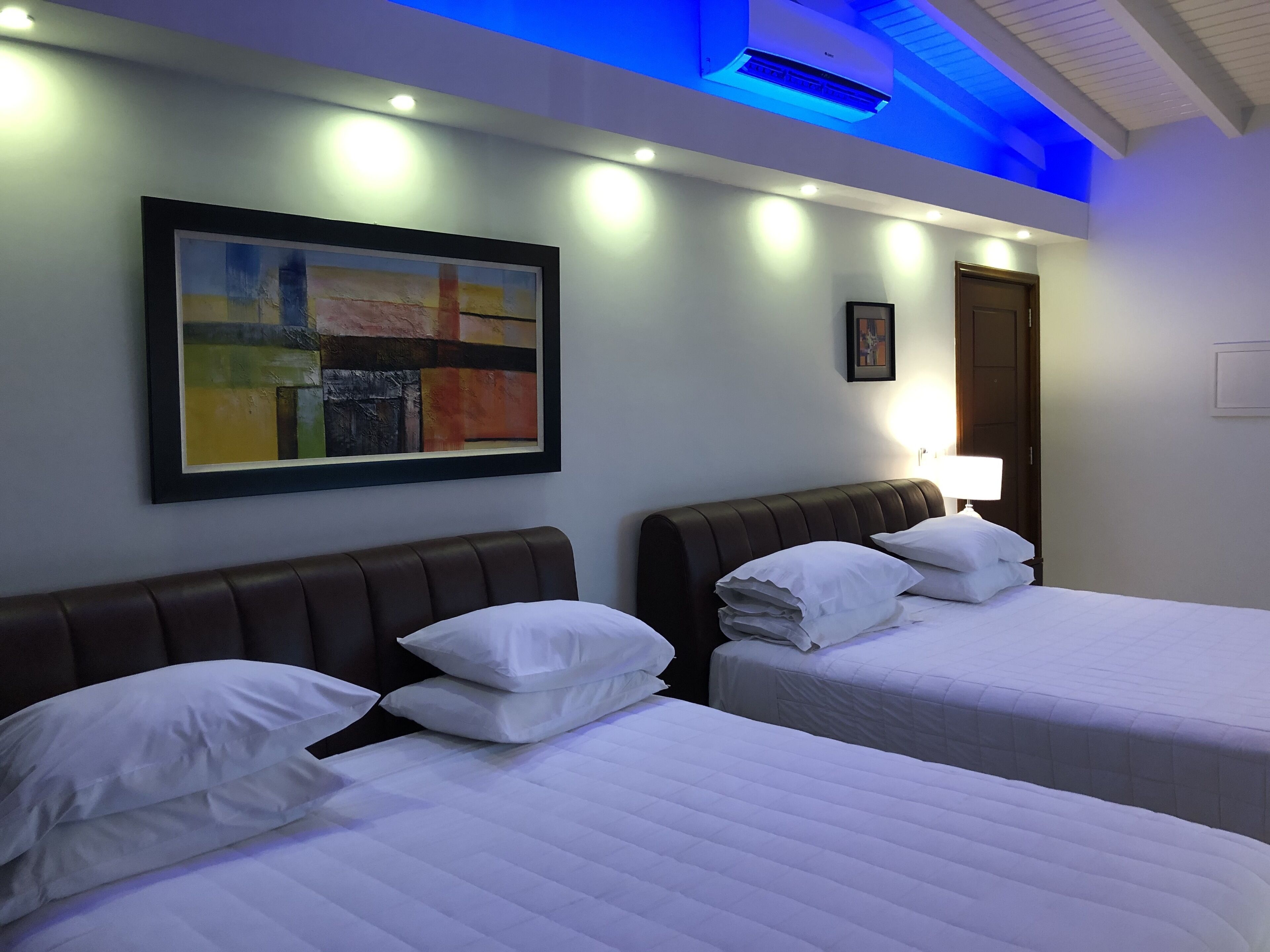 A hotel room with two beds, a painting on the wall, and a ceiling light.