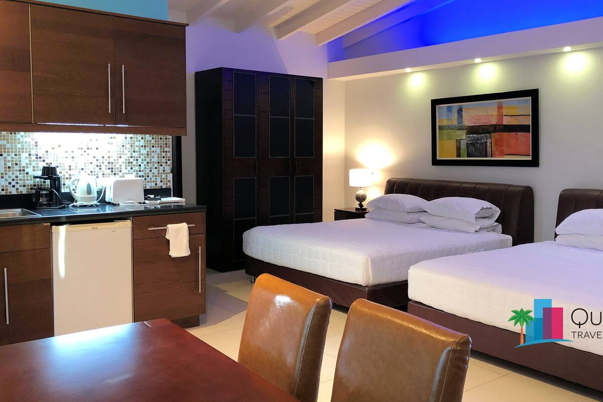 Ein Hotelzimmer mit zwei Betten, einer Küchenzeile, einem Essbereich und einem Bild an der Wand.