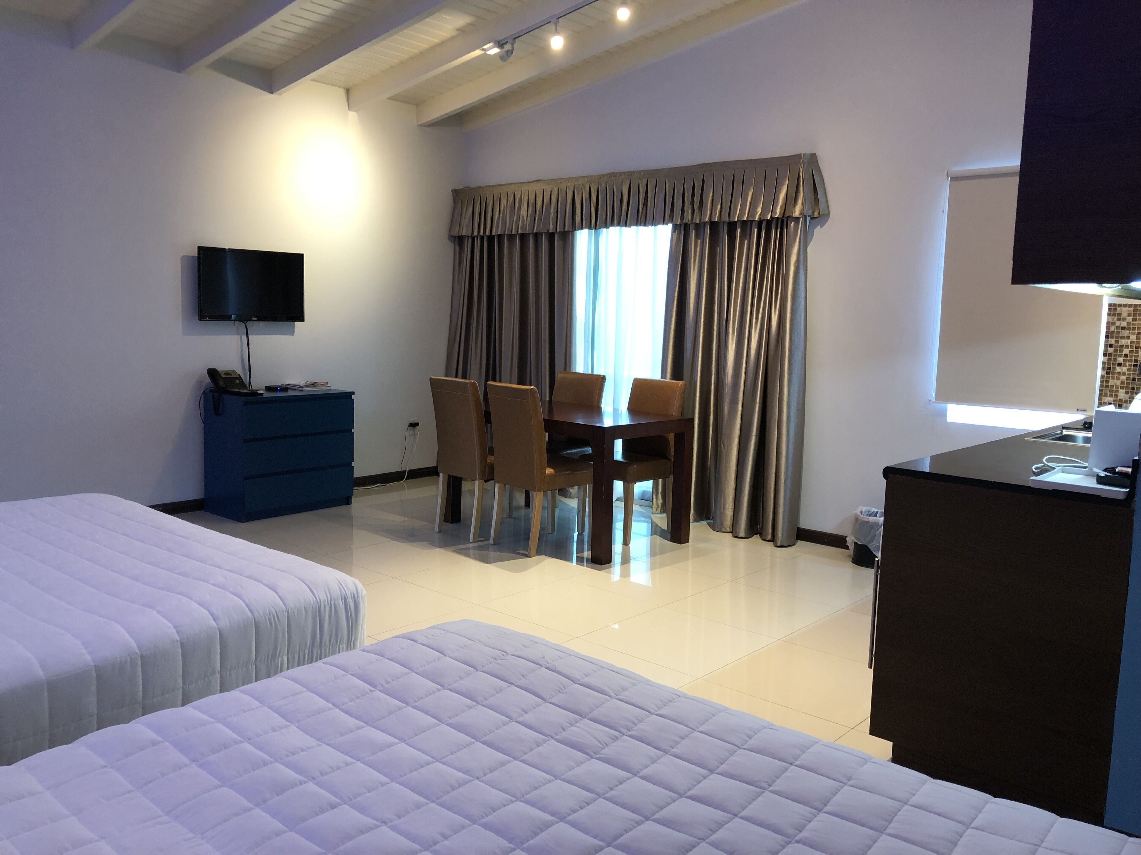 Ein Hotelzimmer mit zwei Betten, einem Schreibtisch mit Computer, einem Stuhl und einem an der Wand montierten Fernseher.
