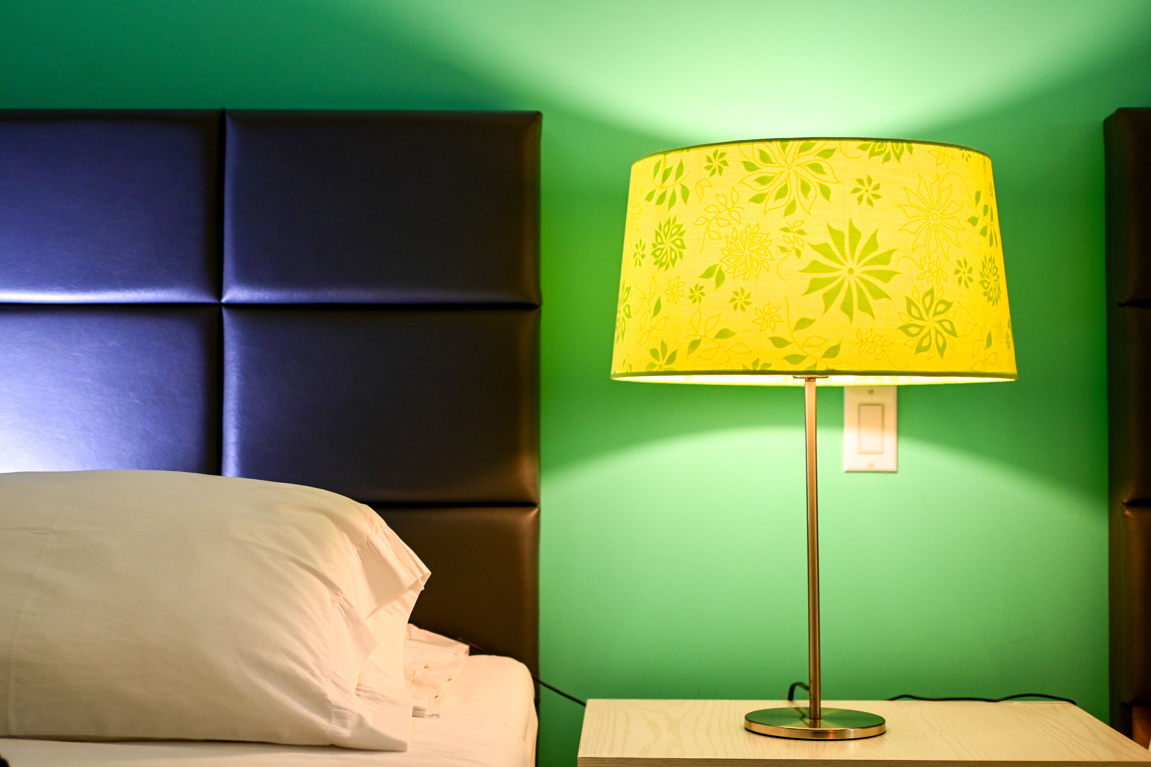 Una cama con un almohadón blanco y una pared verde con un panel texturizado.