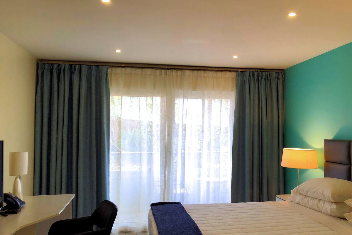 Ein Hotelzimmer mit Bett, Schreibtisch, Stuhl, Lampe und Blick durch das Fenster.