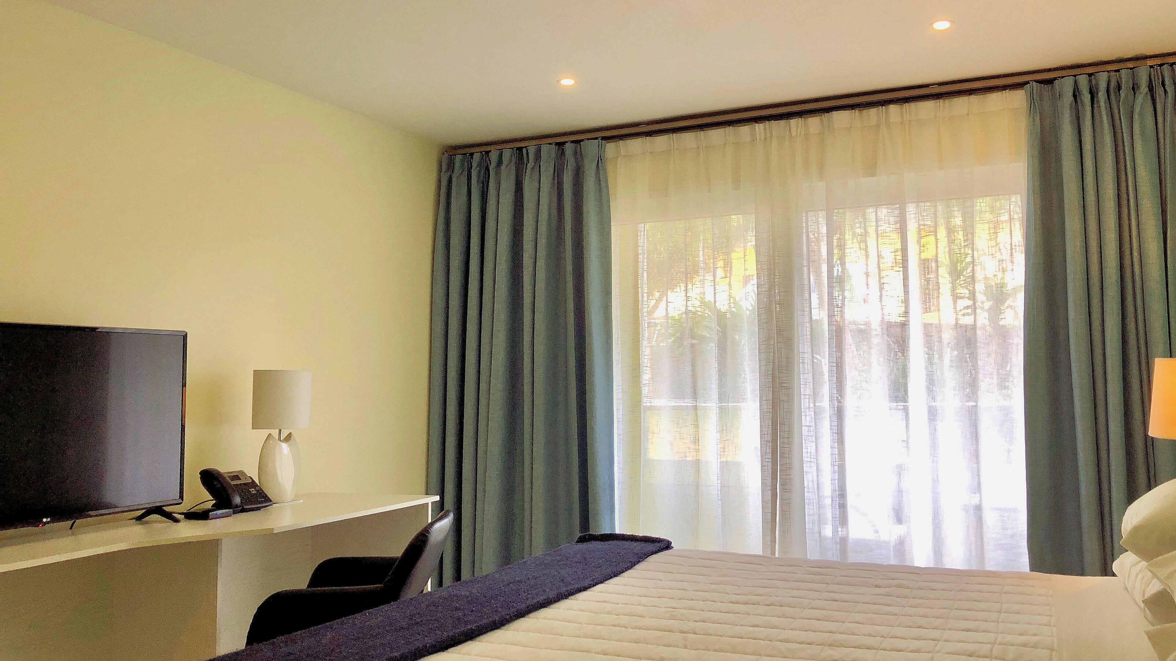 Una habitación de hotel con una cama, un escritorio con televisor, una silla y una ventana con cortinas.