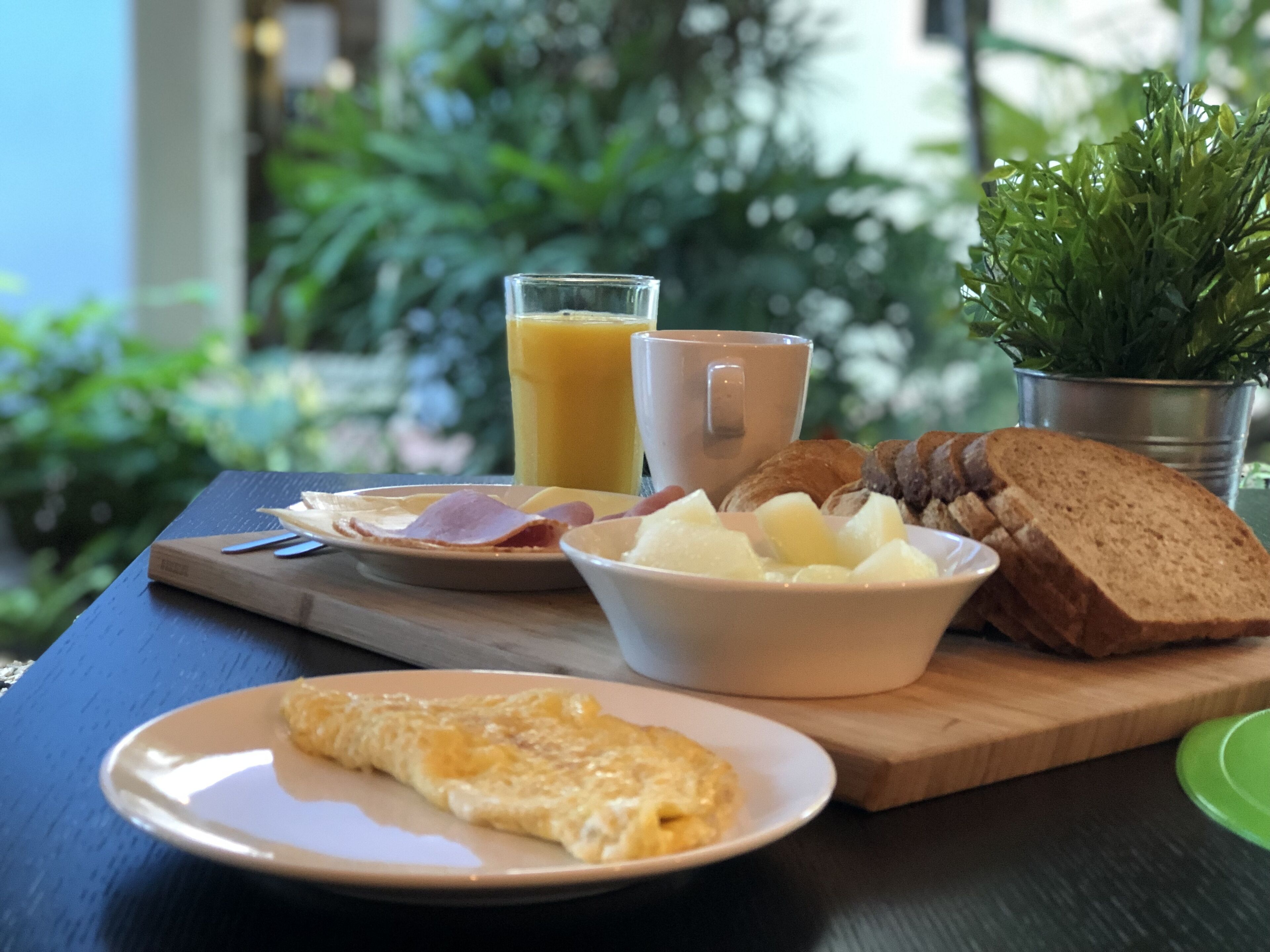 A breakfast table with a plate of eggs, toast, ham, and a glass of orange juice.