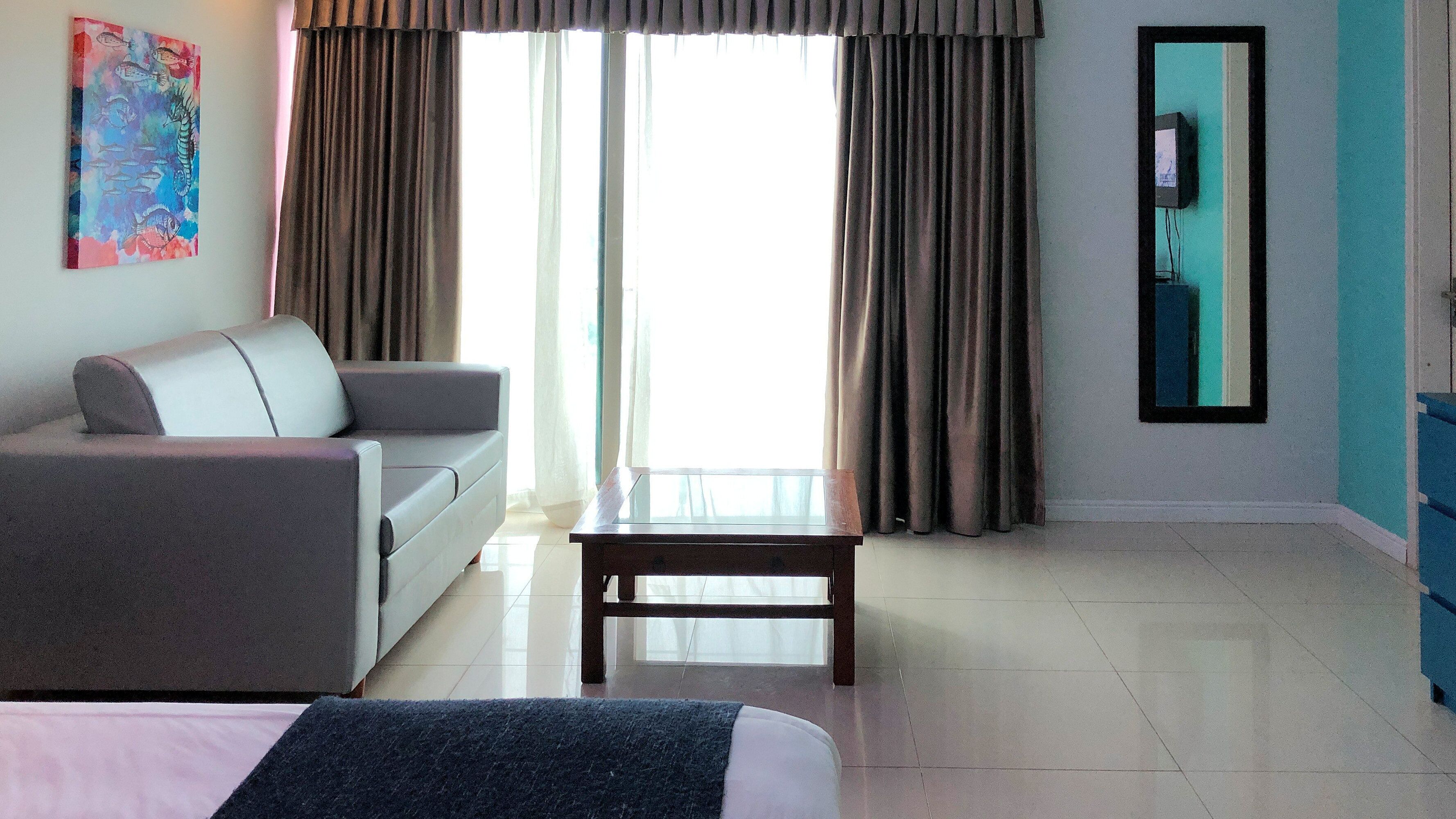 Habitación de hotel con cama, sofá, una mesita, televisor montado en la pared y ventana con cortinas.