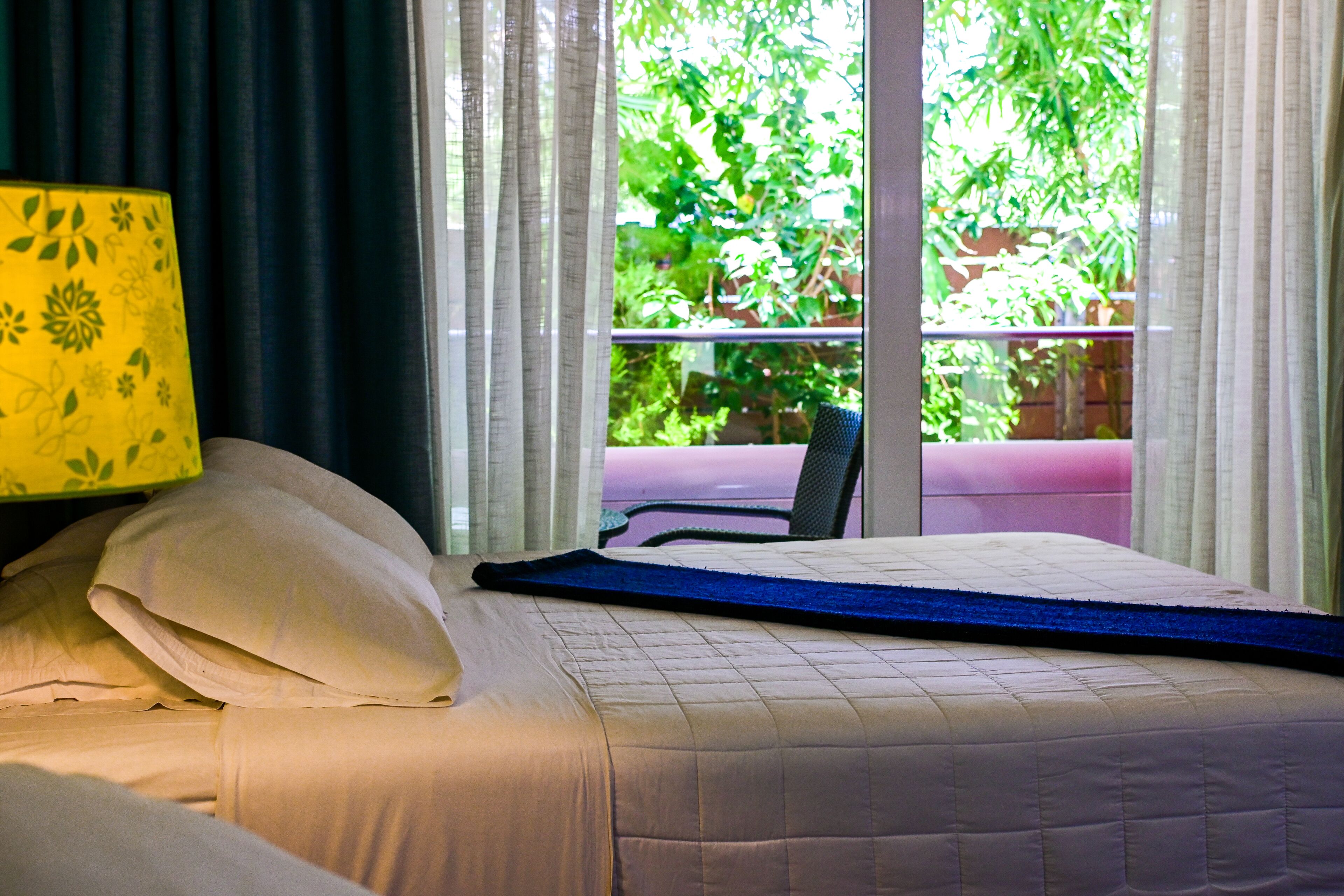 A bed with a blue mattress topper, white pillows, and a yellow floral-patterned lamp.