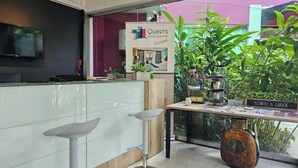 Una moderna recepción con un letrero de Quints Travelers Inn en Curazao, una máquina de café y un pequeño jardín con plantas y un letrero que dice 'Flores & Jardín'.